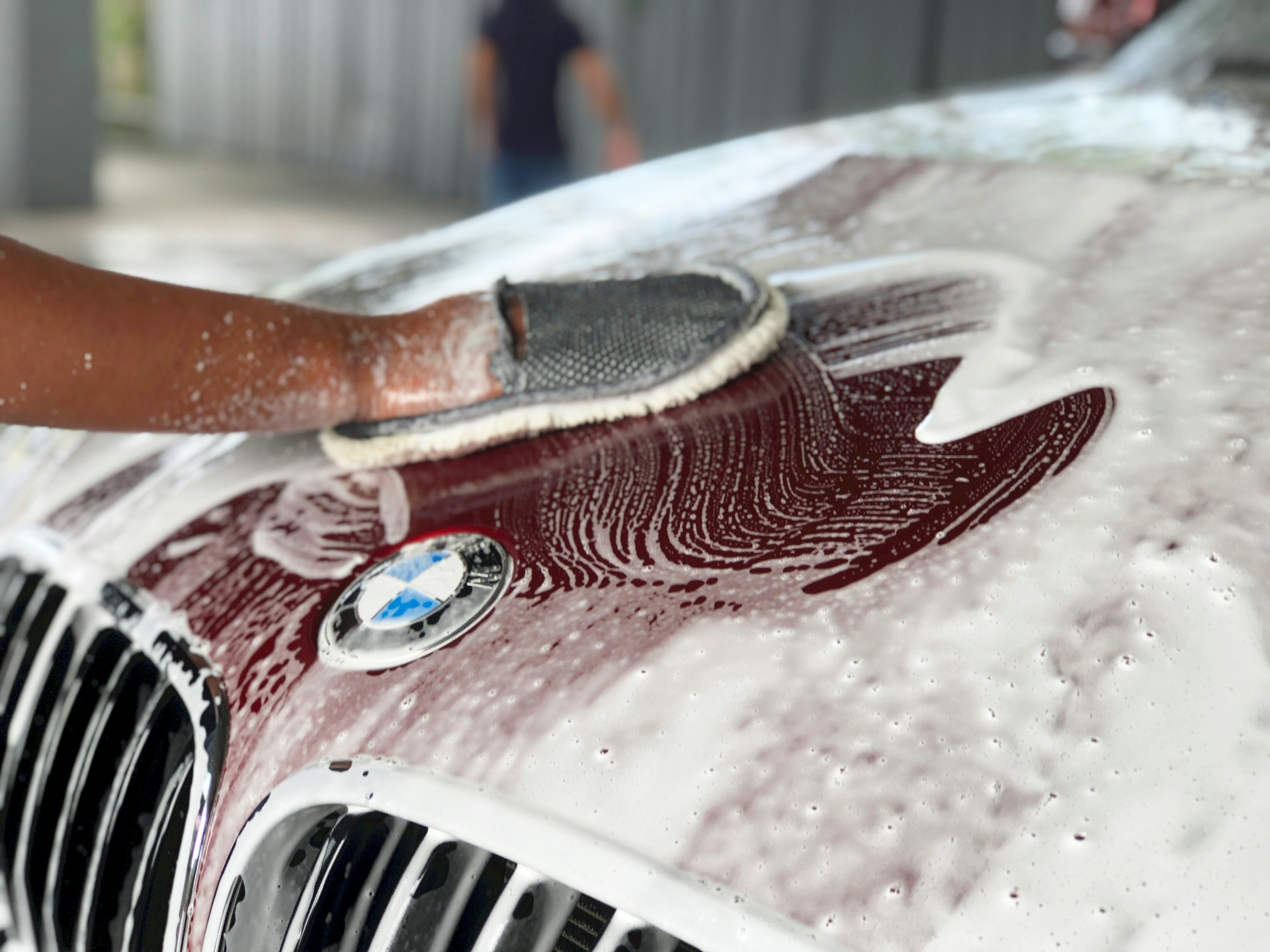 Detailer wäscht ein schwarzes Auto per Hand mit Mikrofaser-Waschhandschuh und Zwei-Eimer-Methode